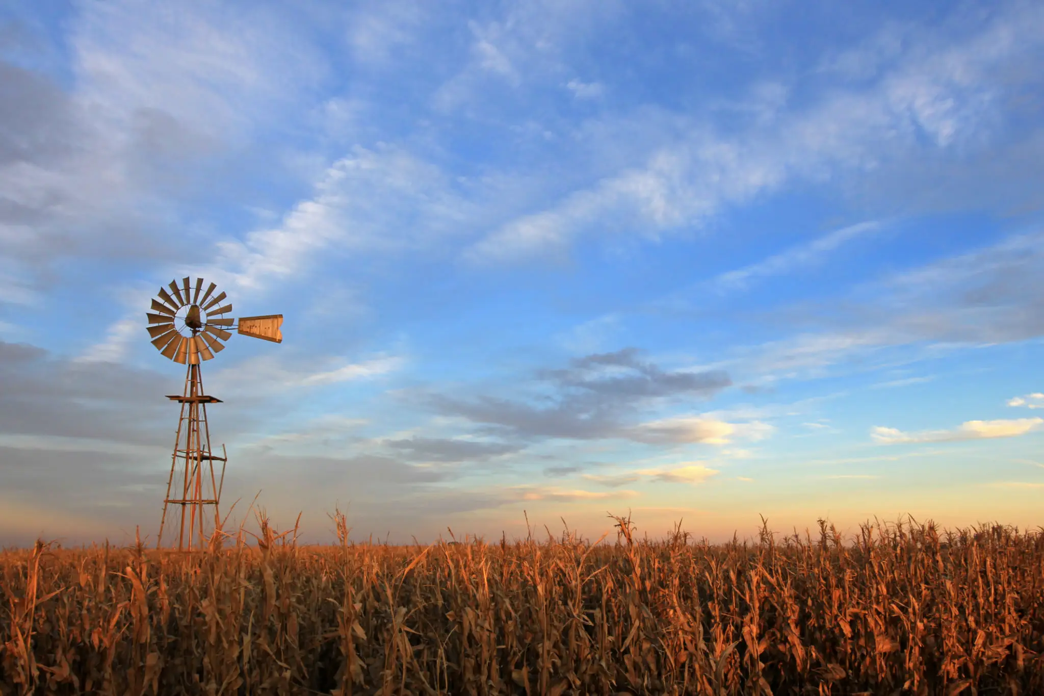 A windmill stands tall beside a field under a partly cloudy sky.